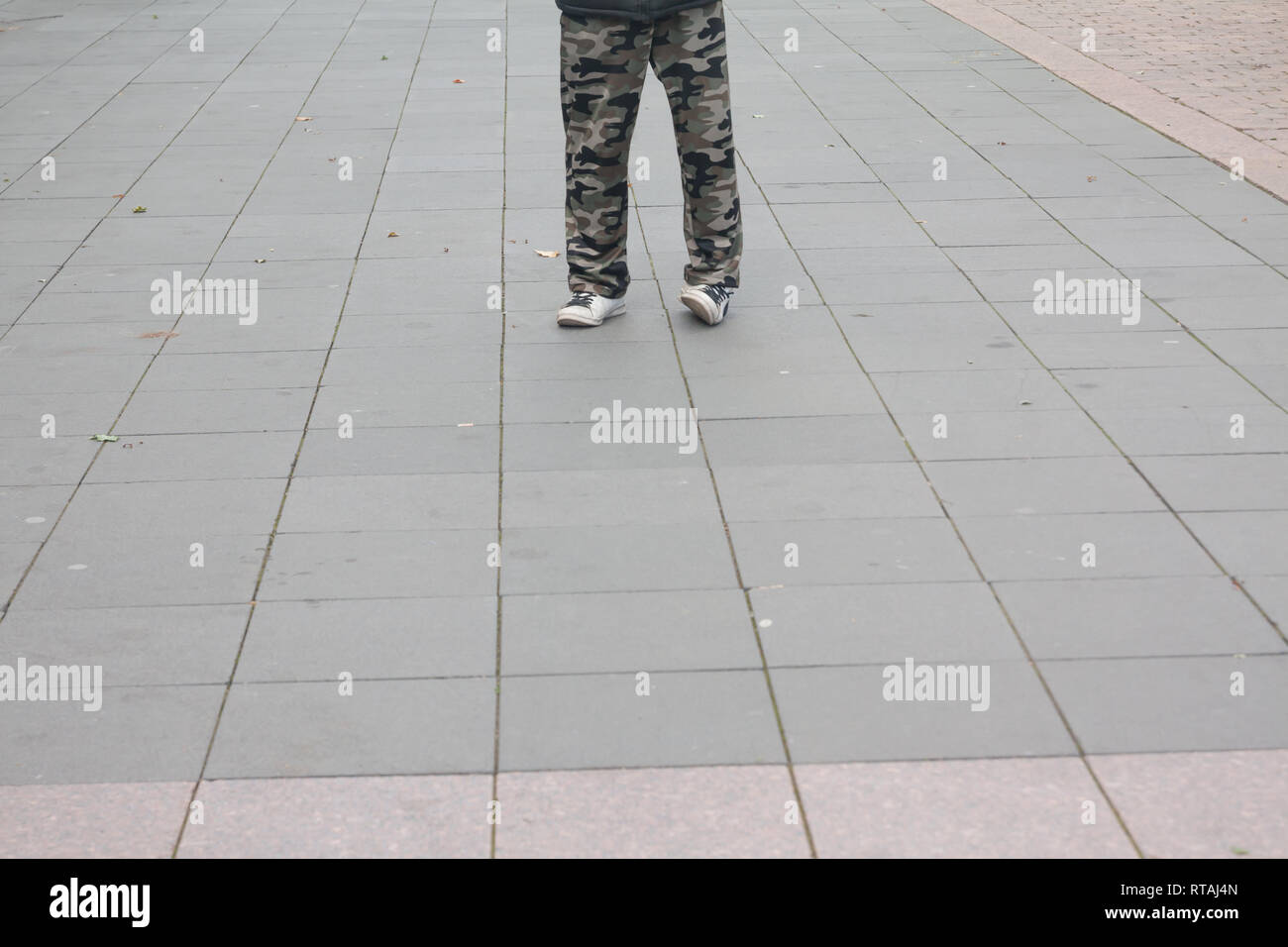 Men feet in old white sneakers and camouflage trousers on pavement on the street. Stock Photo