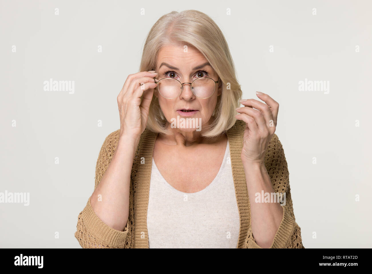 Shocked old woman in disbelief lowering glasses looking at camera Stock Photo