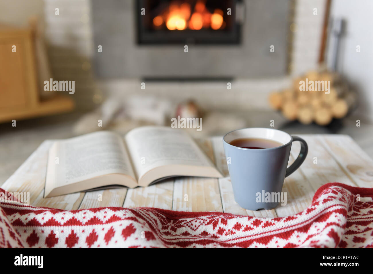 Book and cup of tea near burning fireplace. Hygge concept Stock Photo