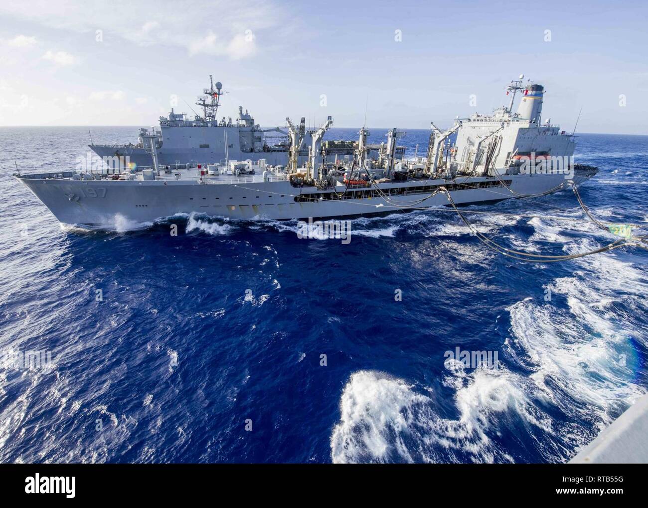 Fleet replenishment oiler USNS Pecos (T-AO 197), center, conducts a vertical replenishment with the Whidbey Island-class amphibious dock landing ship USS Rushmore (LSD 47), top, and the San Antonio-class amphibious transport dock ship USS Anchorage (LPD 23) during a deployment of the Essex Amphibious Ready Group (ARG) and 13th Marine Expeditionary Unit (MEU) in the Pacific Ocea, Feb. 7, 2019. The Essex ARG/13th MEU is a capable and lethal Navy-Marine Corps team deployed to the 7th fleet area of operations to support regional stability, reassure partners and allies and maintain a presence postu Stock Photo