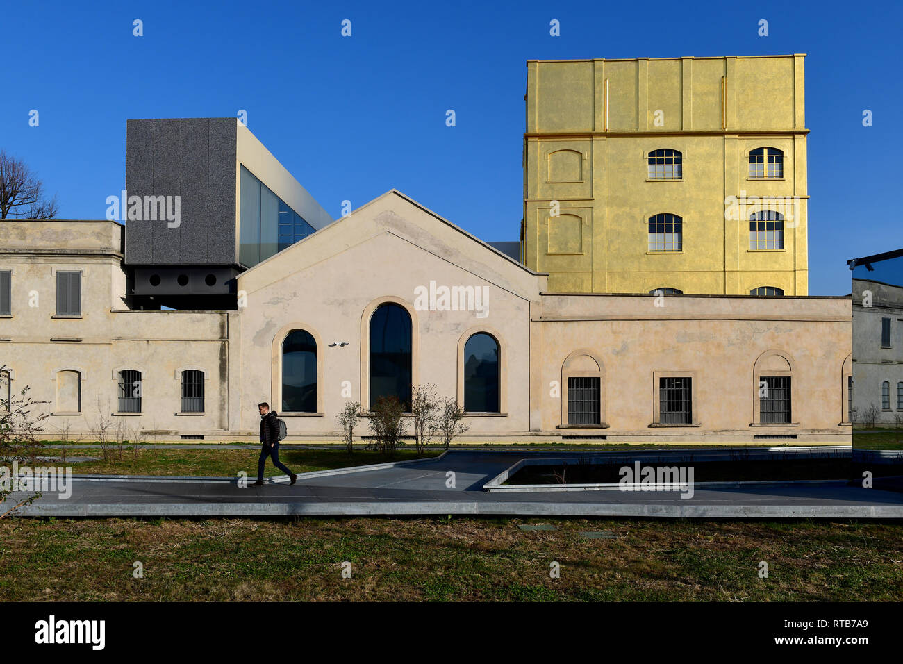 A person walking across Adriano Olivetti square, in the new Symbiosis district. In the background, the Fondazione Prada complex with the Haunted House Stock Photo