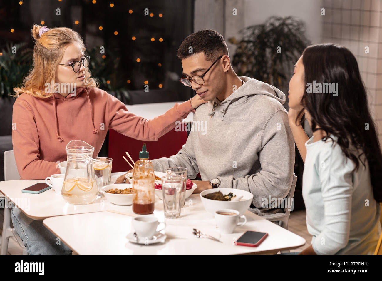 Adorable girls trying to comfort guy by making photos with him. Stock Photo