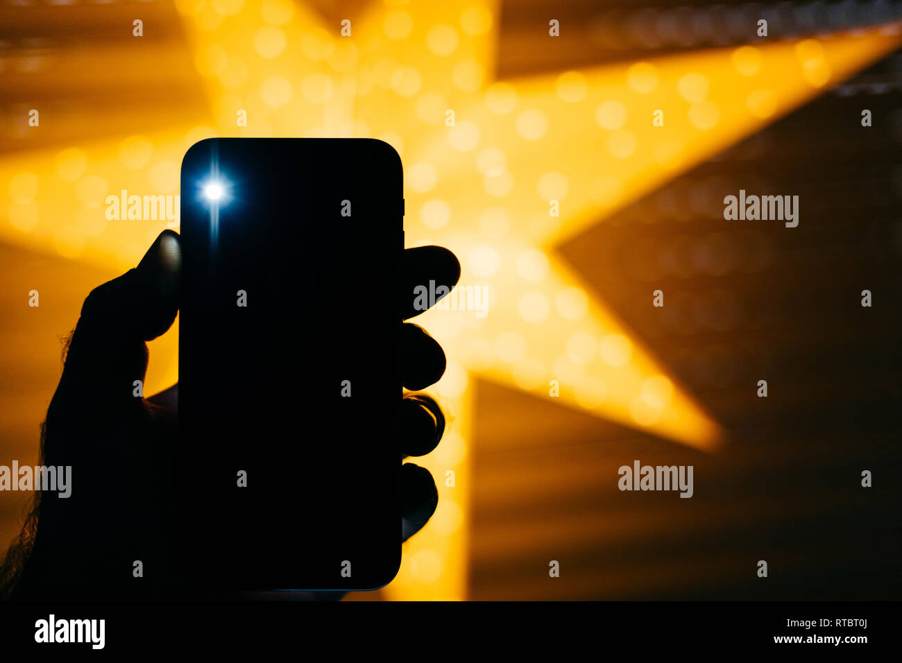 Man holding the new Phone with yellow star bokeh background featuring a blick light from the rear flash and camera - holiday concept  Stock Photo
