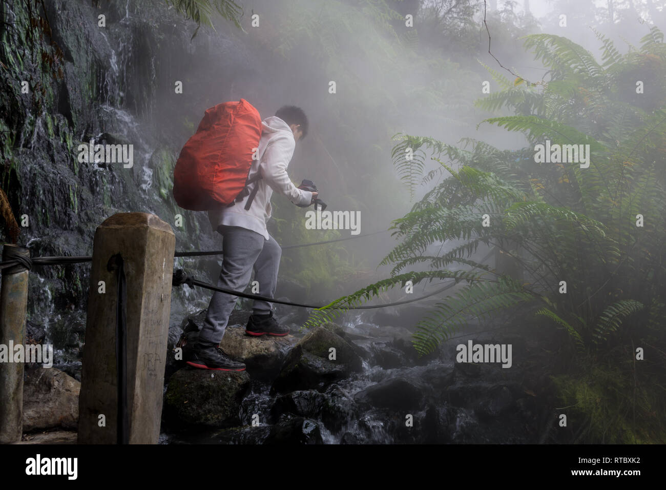 A man is crossing the path of a hot spring stream in the Gunung Gede ...