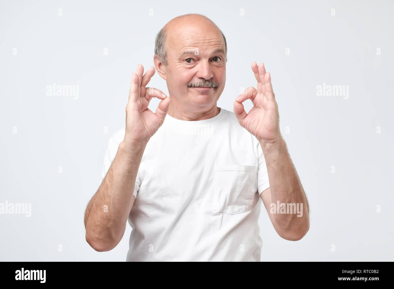 Senior man in white t-shirt showing ok sign. Positive human facial emotion. Stock Photo