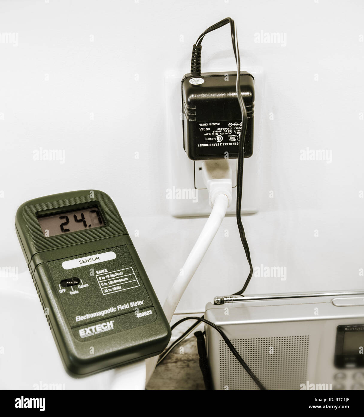 The electromagnetic field meter measures very large amounts of emissions from a small wall transformer (Gauss units). Approximately distance: 20 cm. Stock Photo