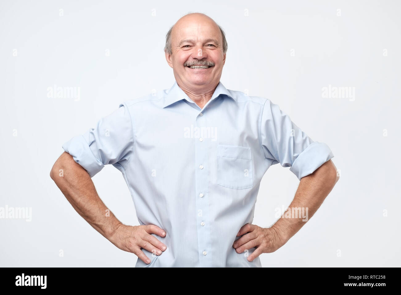 senior handsome man with a proud, satisfied and happy look, with both hands on hips, as if confidently facing a challenge. Akimbo arms pose with a bro Stock Photo
