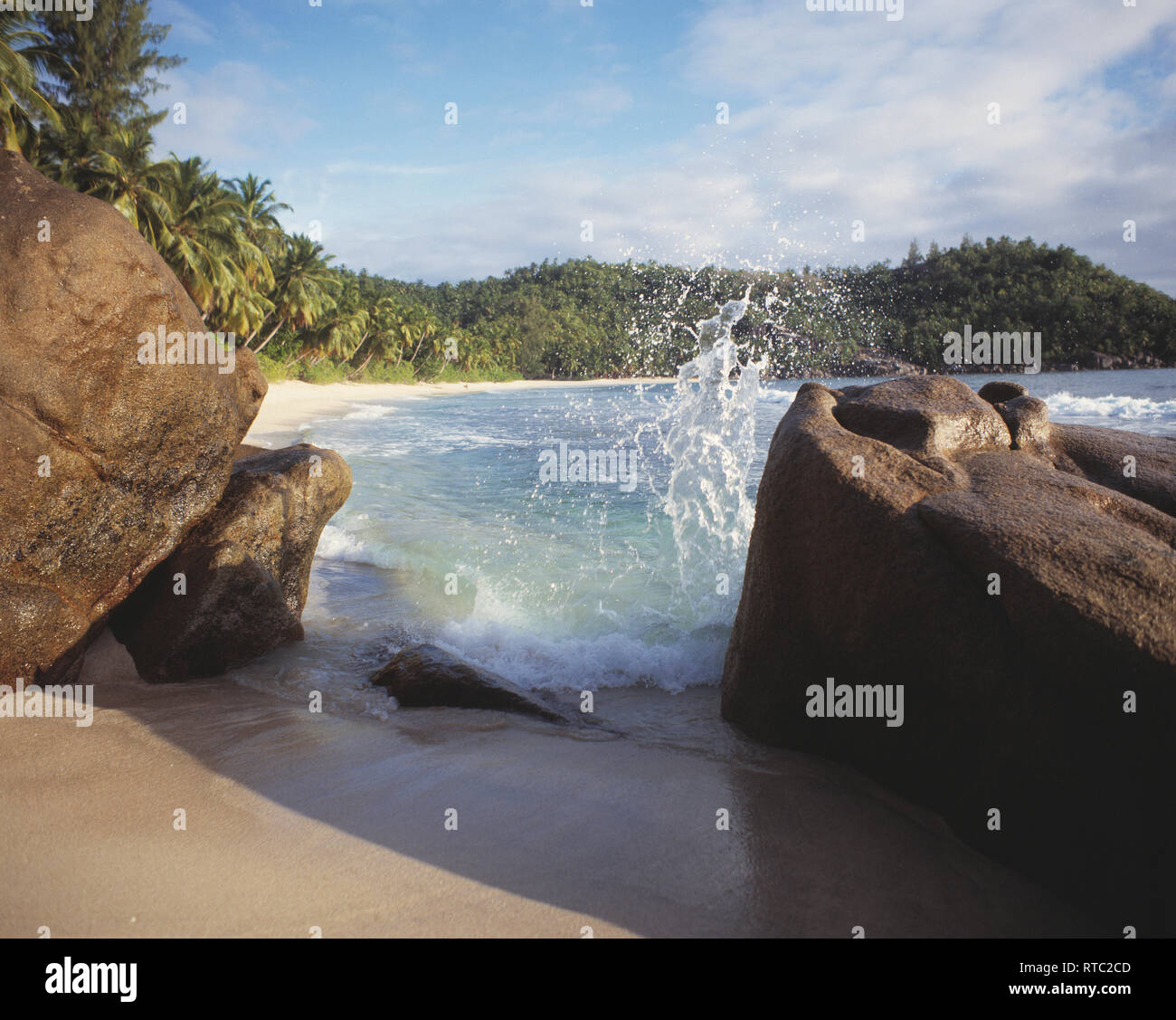 Seychelles. Mahé. Takamaka. Beach scene with wave splashing on boulders. Stock Photo