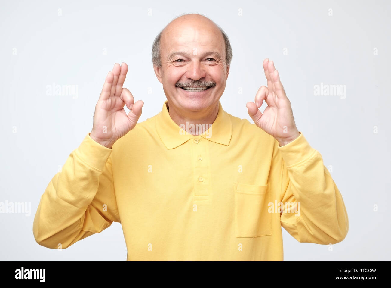 Senior man in yellow shirt showing OK sign. Agreement or making right desicion. Stock Photo