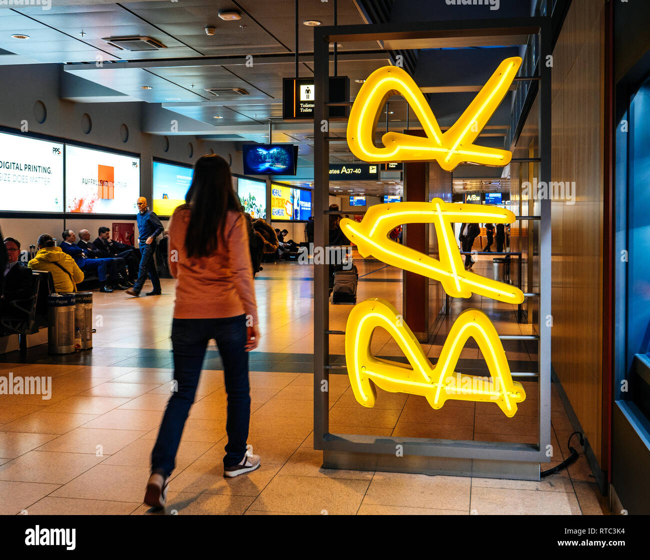 HAMBURG, GERMANY - MAR 22, 2018: People inside Hamburg airport interior waiting for flight, walking neon bar sign Stock Photo