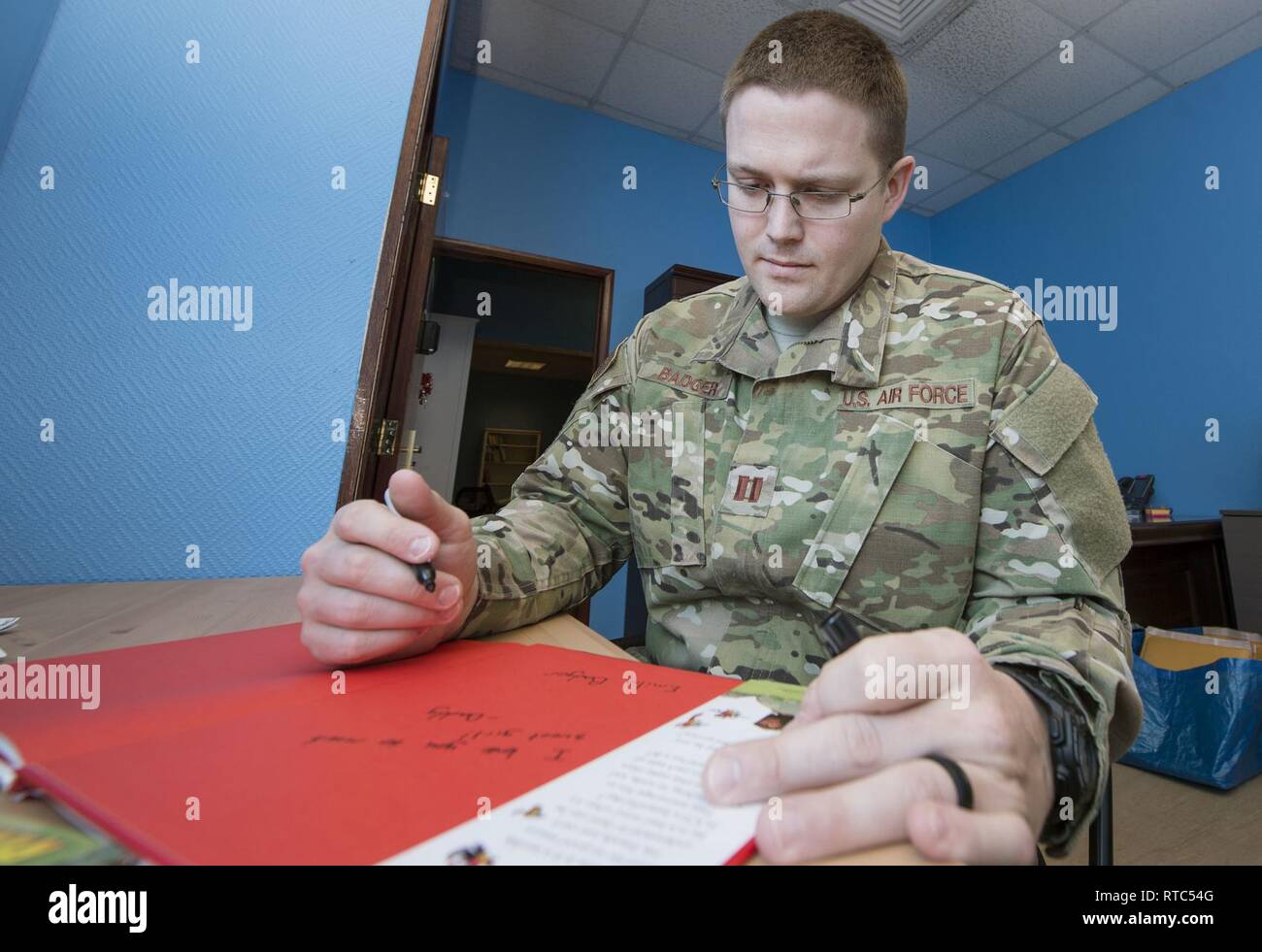 U.S. Air Force Capt. Nathan Badger, 34th Intelligence Squadron flight commander, writes messages to his children in a book as part of United Service Organizations (USO) Qatar’s Reading Program Feb. 8, 2019, at Al Udeid Air Base, Qatar. The USO reading program allows service members to record themselves reading books to send back to their children. Program participants can write messages in the books and send them to their children along with the video recording. Stock Photo