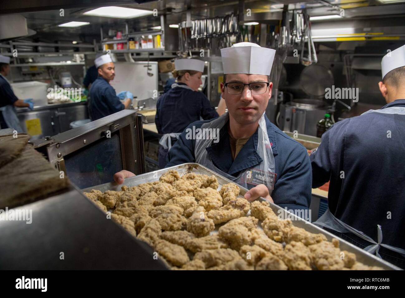 U.S. Navy Hospital Corpsman 1st Class Nicholas Lotito, from Liverpool, New York, places chicken wings into an oven during a First Class Petty Officer Association hosted pizza night aboard the guided-missile destroyer USS Stockdale (DDG 106) in the Arabian Sea, Feb. 9, 2019. The Stockdale is deployed to the U.S. 5th Fleet area of operations in support of naval operations to ensure maritime stability and security in the Central Region, connecting the Mediterranean and the Pacific through the western Indian Ocean and three strategic choke points. Stock Photo