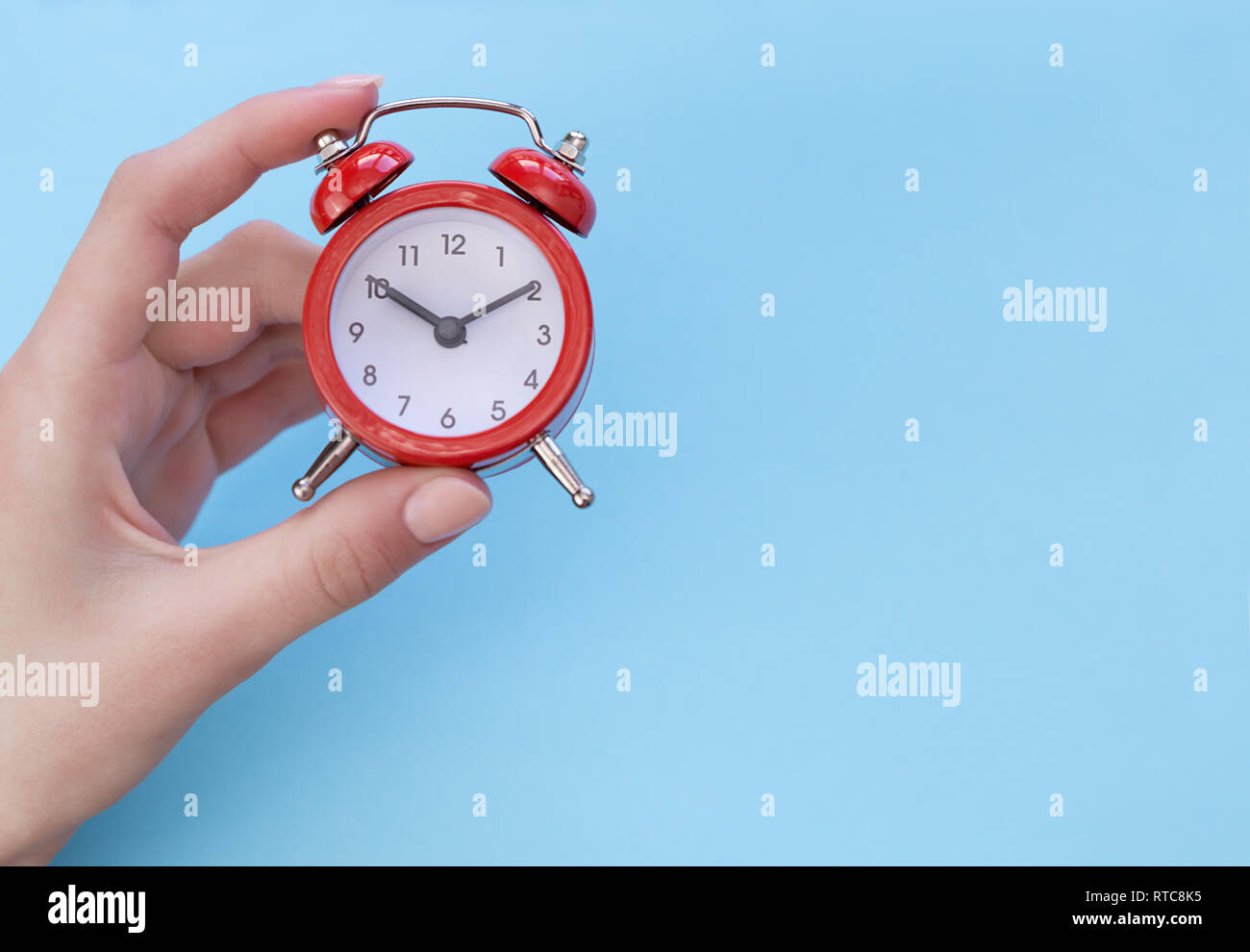 girl holding a red retro alarm clock showing ten o'clock ten minutes on the dial, on a blue background. Concept - time is money Stock Photo