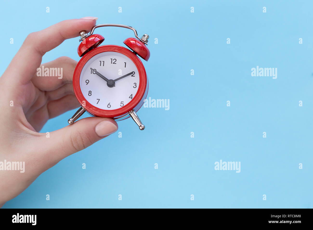 girl holding a red retro alarm clock showing ten o'clock ten minutes on