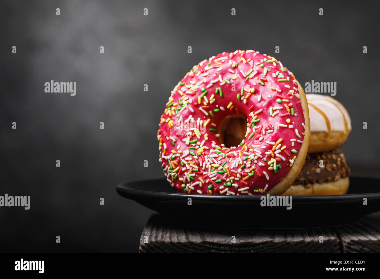 Several fresh donuts in a black ceramic plate on a wooden table with copy space Stock Photo