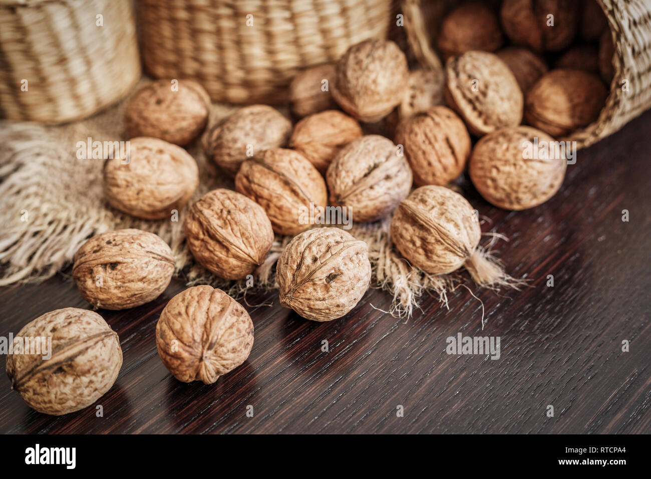 Close-up view of whole walnuts scattered on a dark wooden table with rustic background, selective focus. Healthy food concept. Stock Photo