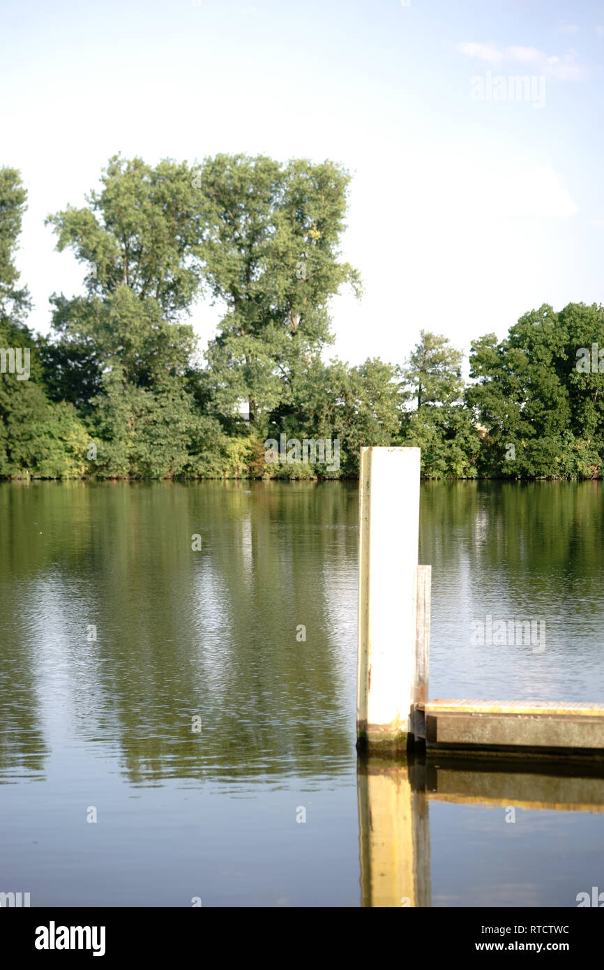 A steel pier or jetty is reflected along with the river bank. Stock Photo