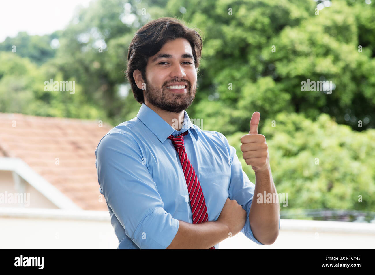 Smart latin businessman with beard showing thumb up outdoors Stock Photo