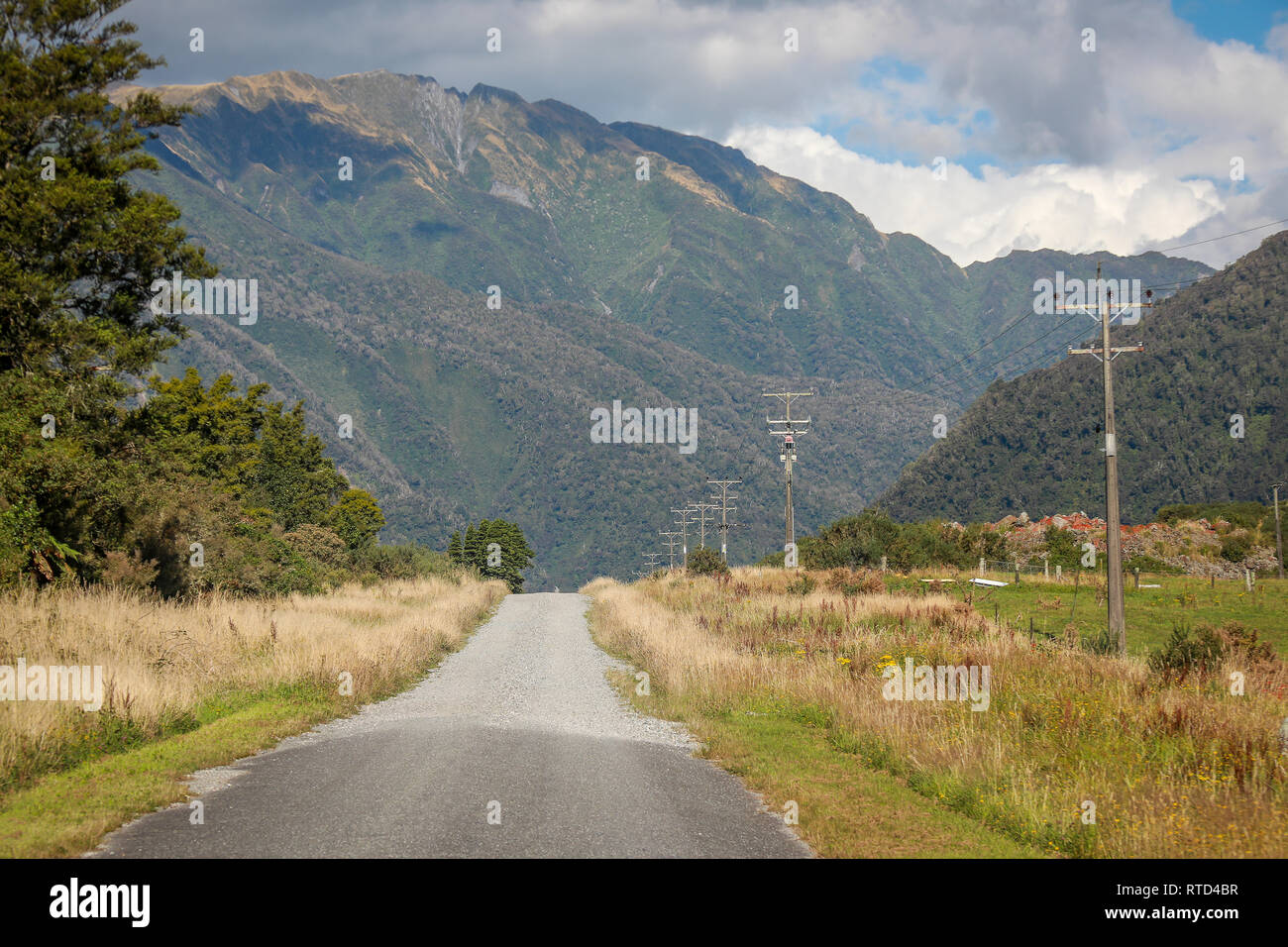 Country gravel road in to the mountains with electricity pylons and wires near Franz Josef New Zealand South Island west coast Stock Photo