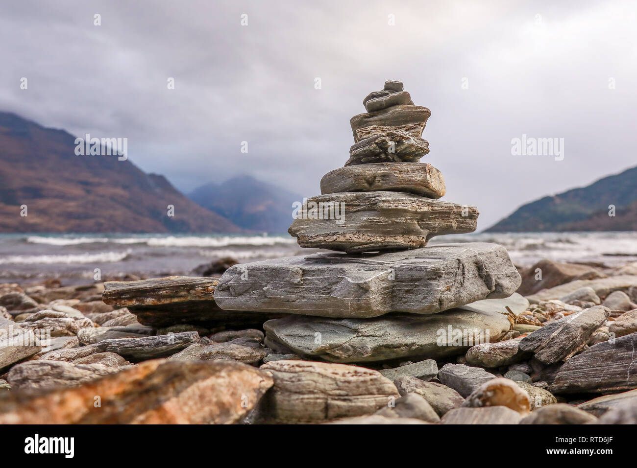 A small cairn of stones on the shore of Lake Wakatipu, Queenstown. New Zealand South Island with Cecil Peak and Walter Peak in the background Stock Photo