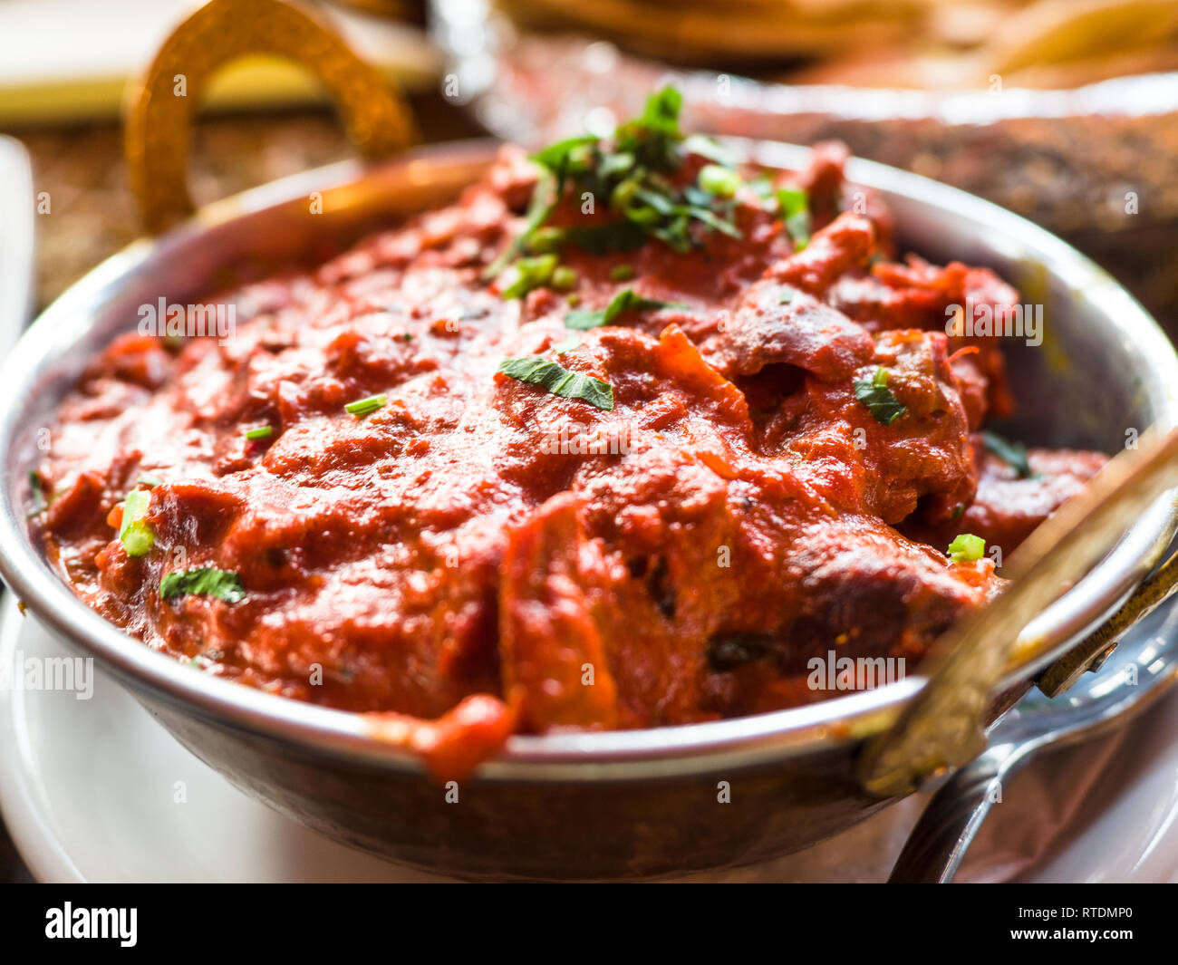 Indian Food or Indian Curry in a copper brass serving oriental bowl, pieces of chicken fillet in curry sauce ingredients in a pan with the old table Stock Photo