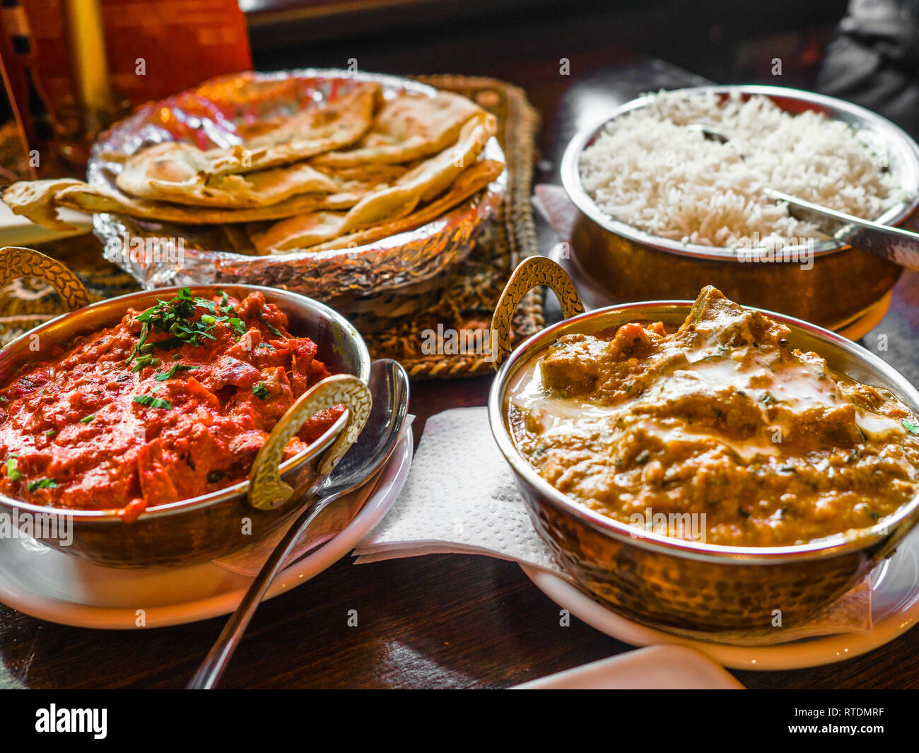 Indian Food or Indian Curry in a copper brass serving oriental bowl, pieces of chicken fillet in curry sauce ingredients in a pan with the old table Stock Photo
