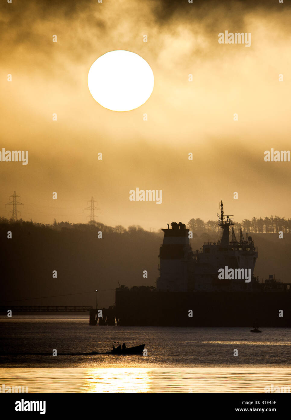Whitegate, Cork, Ireland. Ist March, 2019. Fishermen head out to check their pots at sunrise, passing the superstructure of the crude oil tanker Searanger being unloaded at the Whitegate Oil Refinery in Co. Cork, Ireland. Credit: David Creedon/Alamy Live News Stock Photo