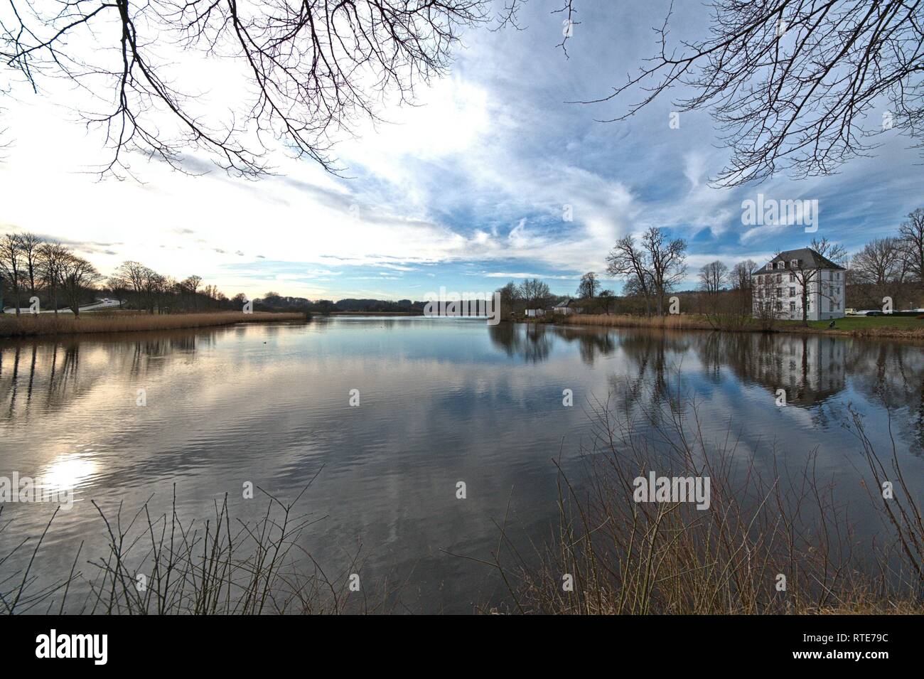 Schleswig, Deutschland. 23rd Feb, 2019. Spatwinter with the feeling of spring at the moat of Gottorf Castle in Schleswig. The sky is reflected in the water. Right in the picture the cavalier house in which, among other things, the administration of the castle is housed. | usage worldwide Credit: dpa/Alamy Live News Stock Photo