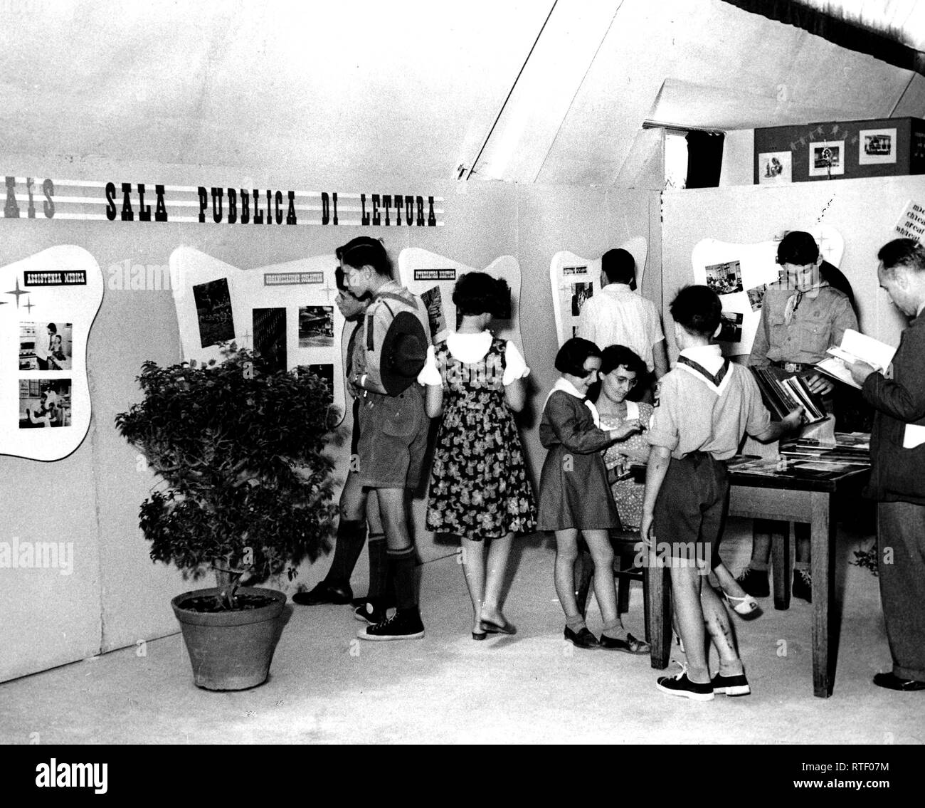 The exhibit was on the subject of 'the Amerian school.' Here children are interesting themselves in the photographic exhibit while others are asking the librarian (seated) questions about one of the most popular items, the 'Basic Science Education Series.' Stock Photo