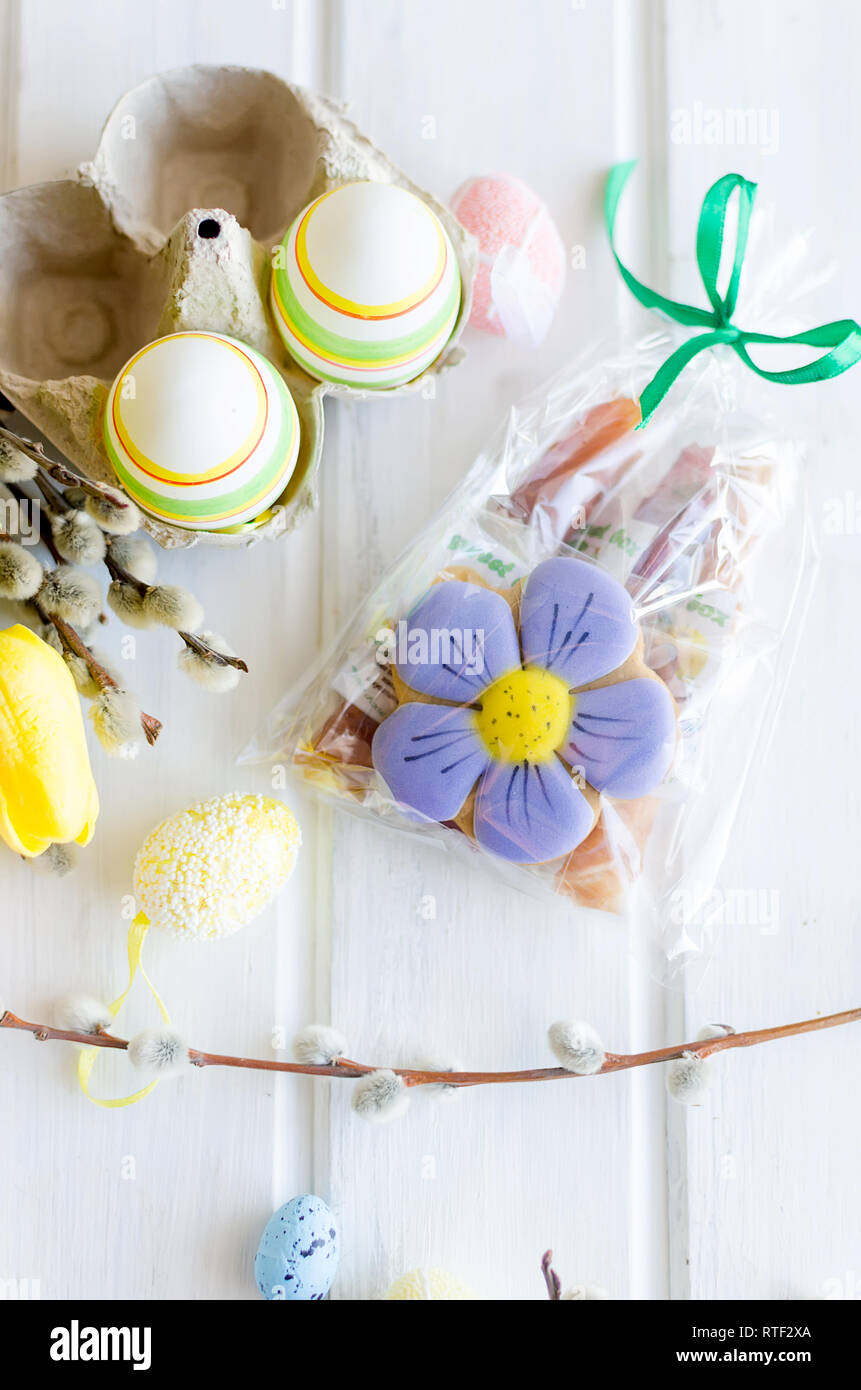 yellow tulips, ginger cookies, willow twigs, decorative eggs in a tray laid out on a white old wooden table, easter holiday background with sweets, fl Stock Photo