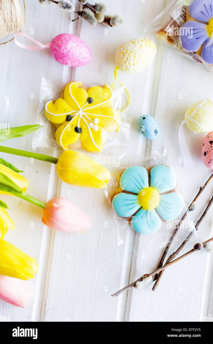 yellow tulips, ginger cookies, willow twigs, decorative eggs in a tray laid out on a white old wooden table, easter holiday background with sweets, fl Stock Photo