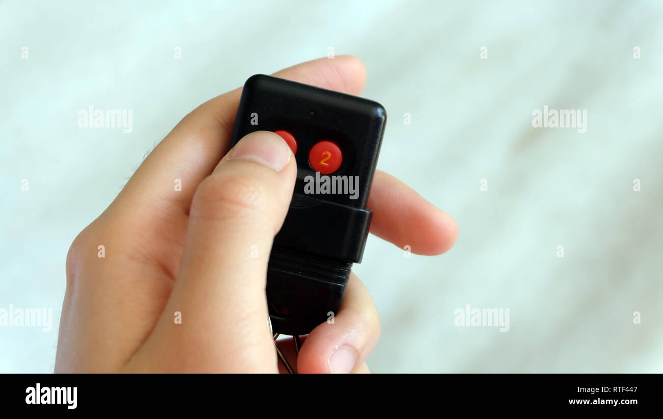 Hand holding and pressing button of an auto gate remote control device. Stock Photo