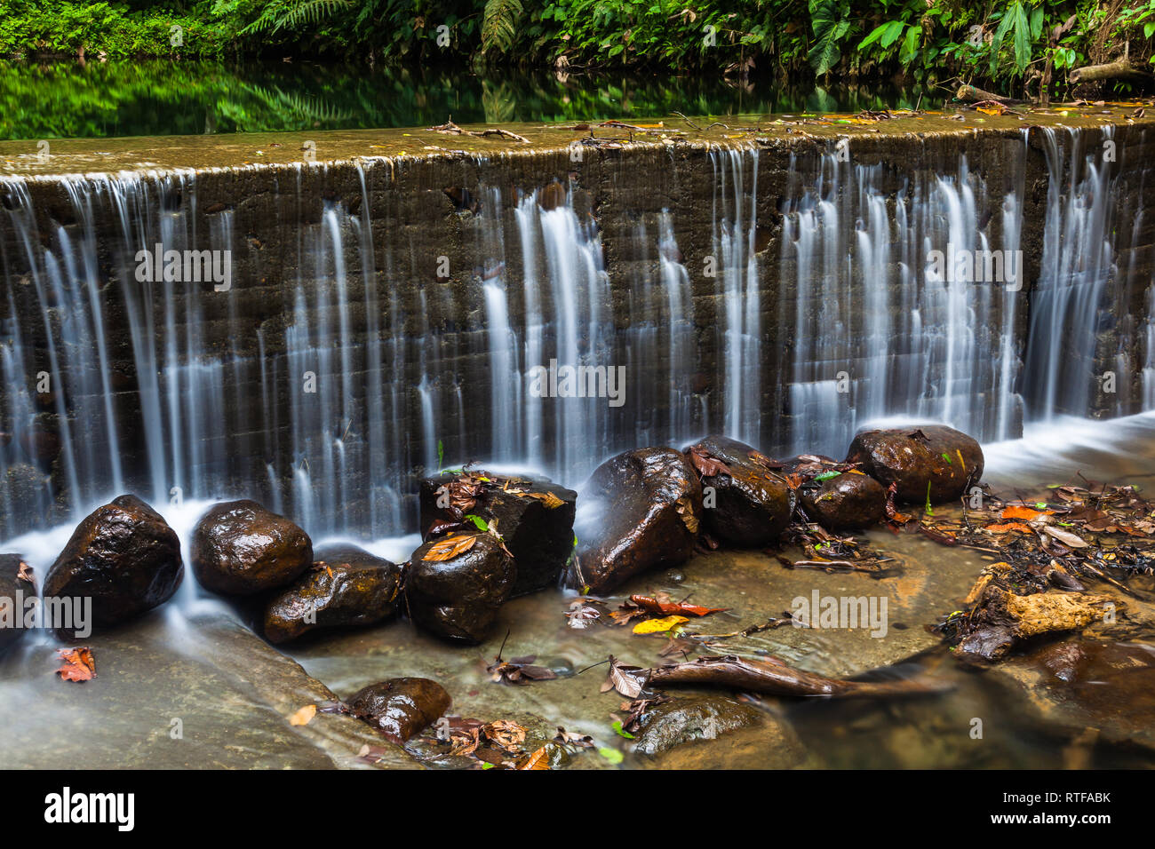 Small artificial waterfall in a beautiful river surrounded by jungle vegetation Stock Photo