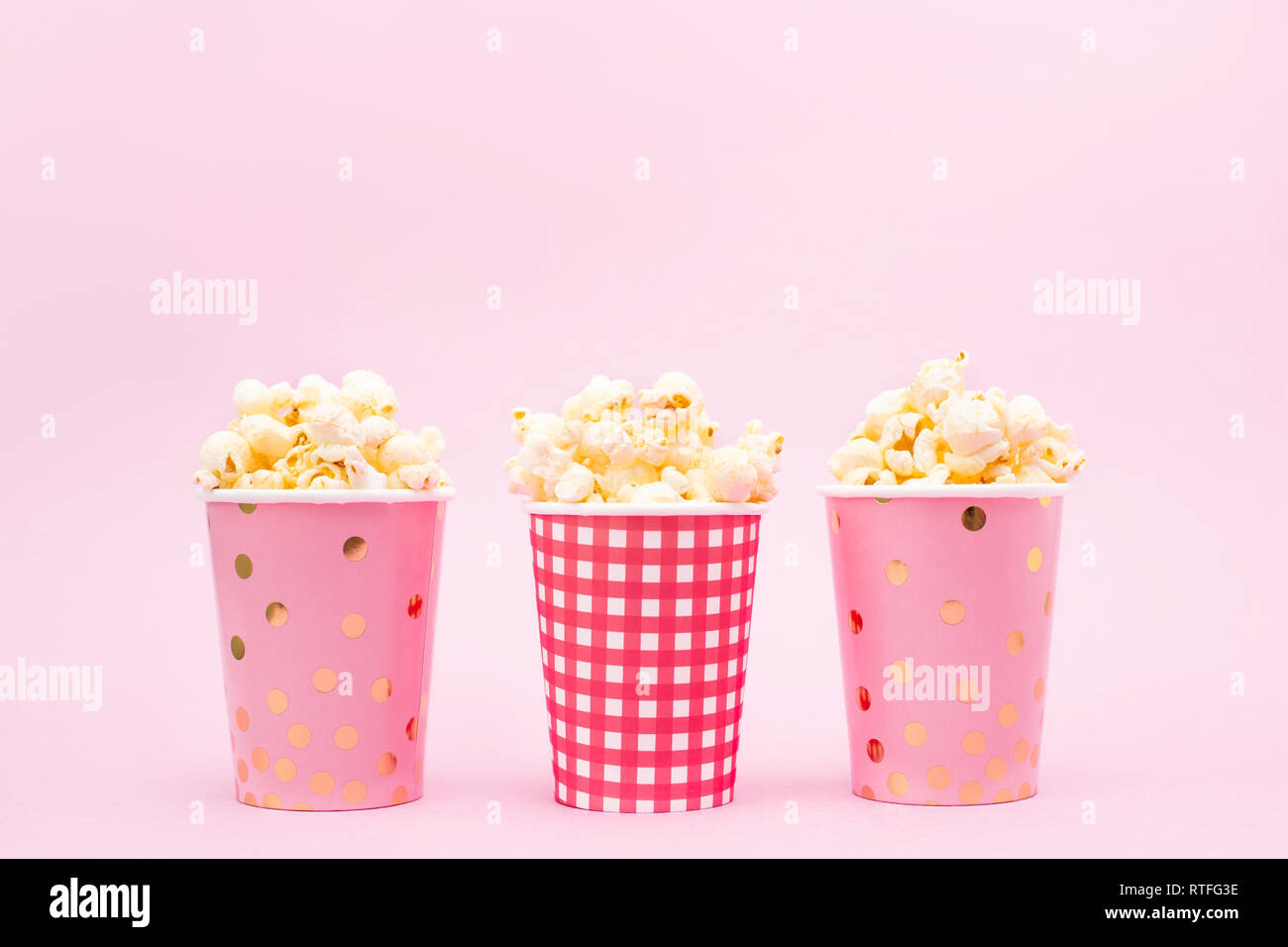 several cups of popcorn on a pink background Copy space Stock Photo