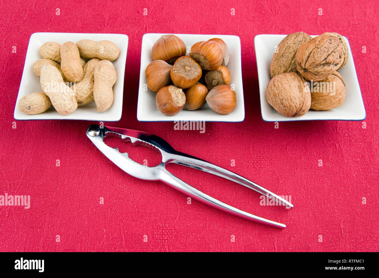 walnuts, hazelnuts and peanuts in three bowls on red background Stock Photo