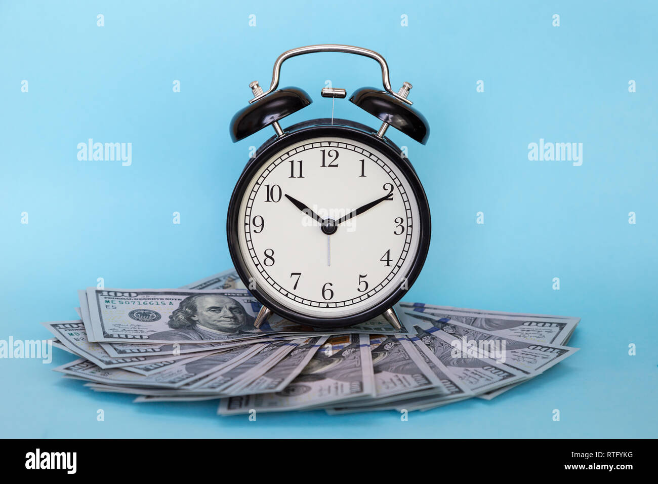 Black retro alarm clock and dollars on a blue colored background. Concept - time is money Stock Photo