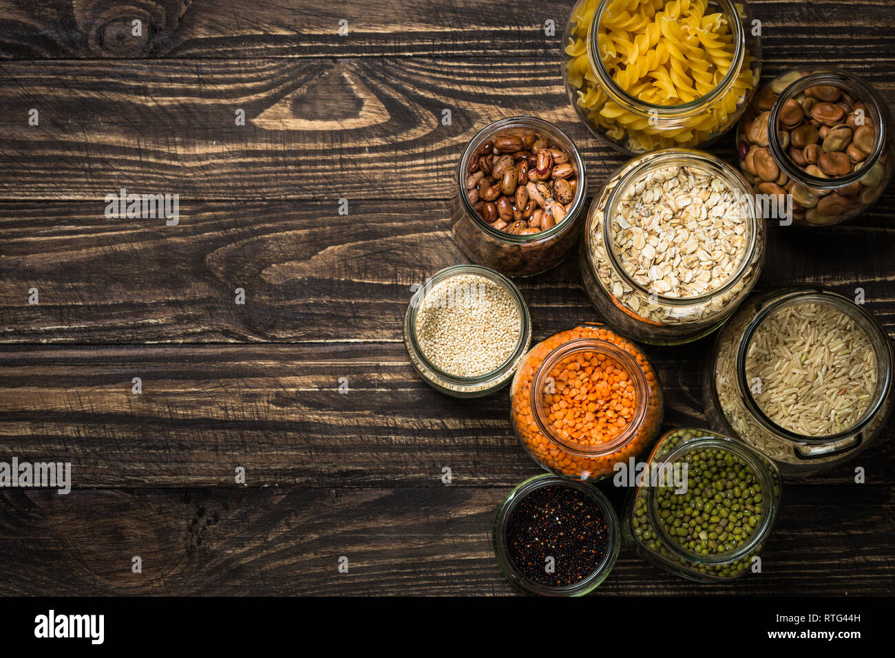 Cereals, Legumes, and beans in glass jars on dark wooden table. Stock Photo