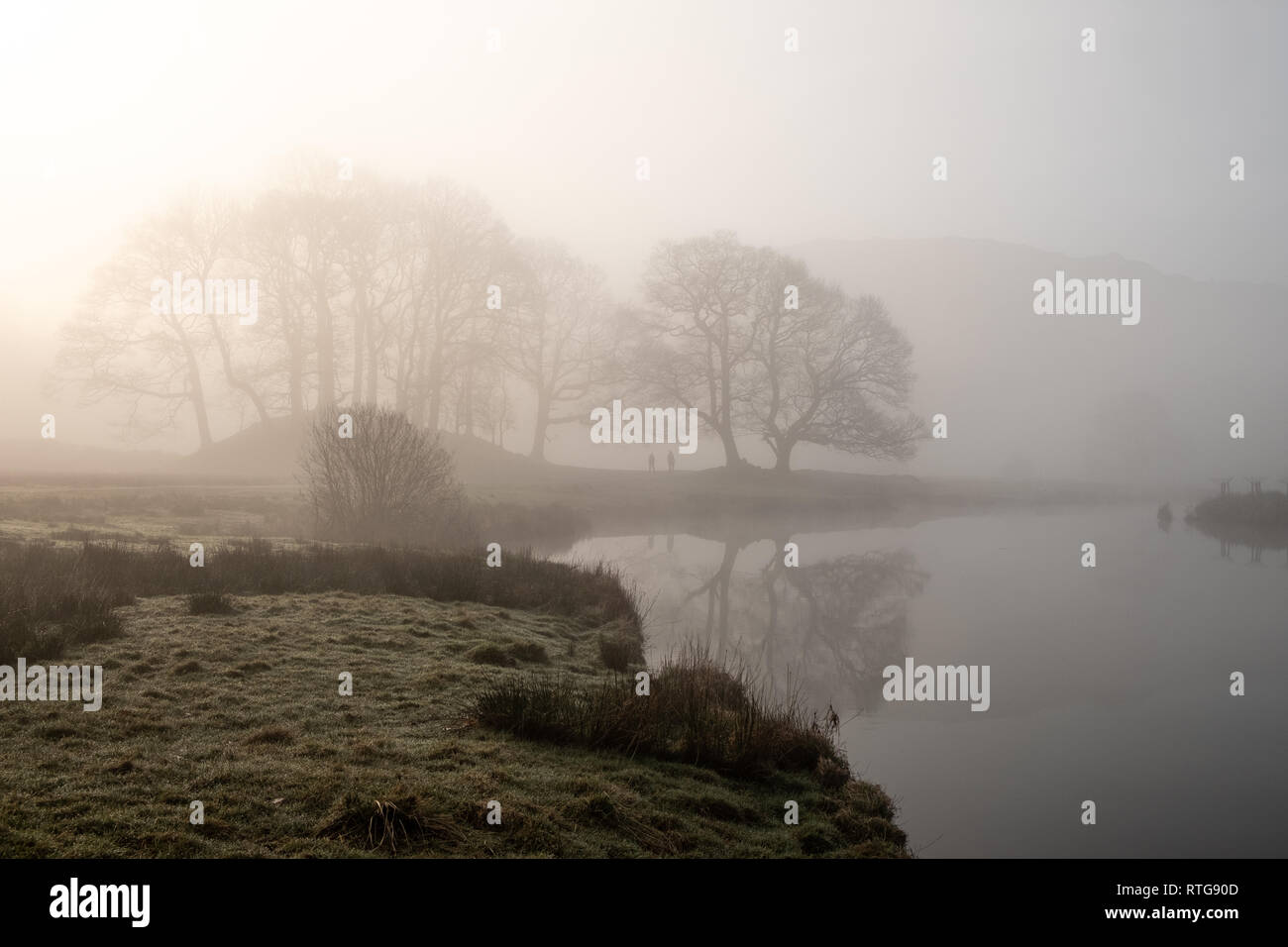 Early morning mist hanging over the River Brathay between Elterwater and Skelwith Bridge. Two people seen in the distance. Lake District, UK Stock Photo