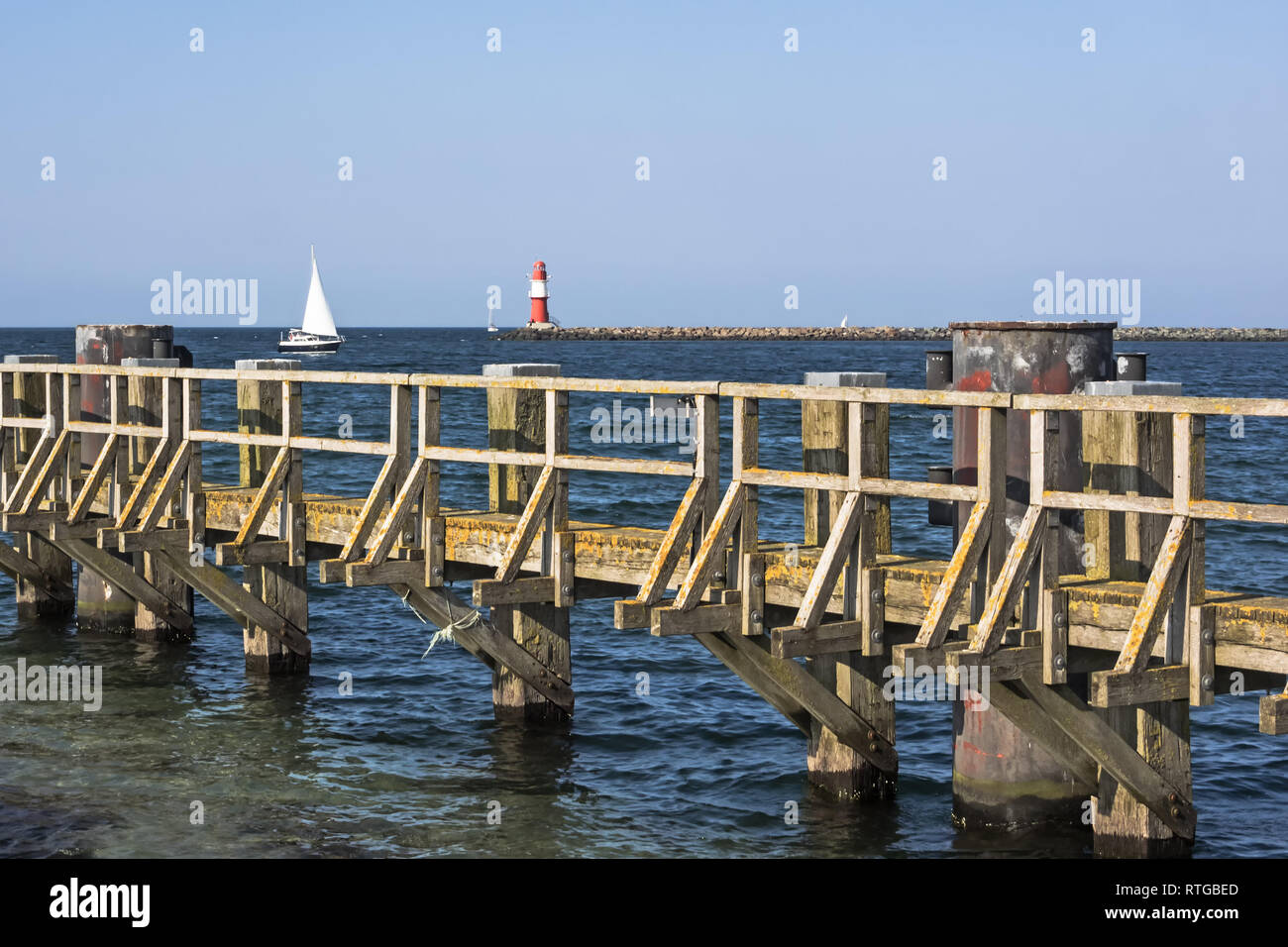 Baltic Sea with wooden pier, lighthouse and sailing ship at Rostock Warnemuende, Germany Stock Photo
