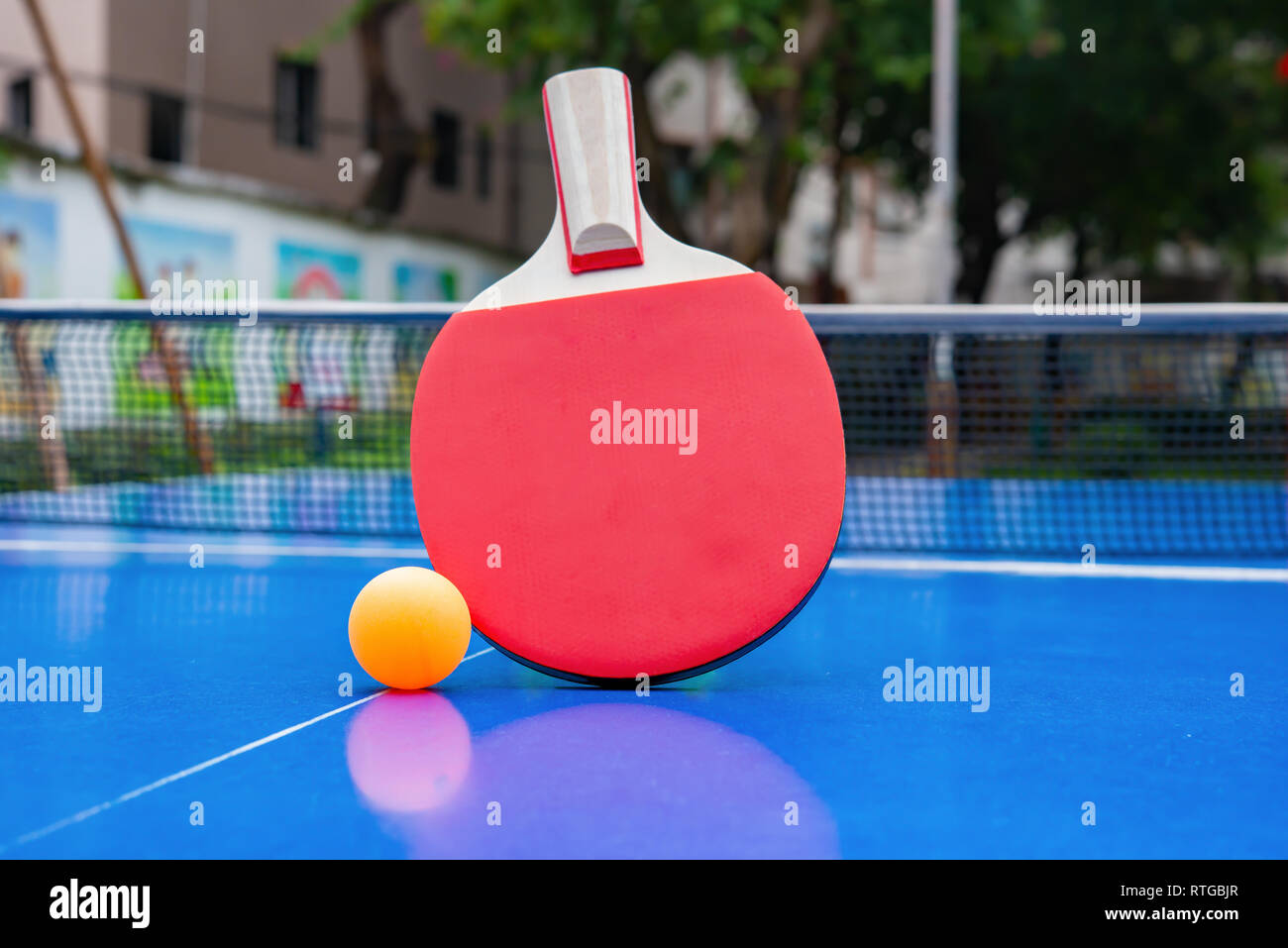 pingpong racket and ball and net on a blue pingpong table in a park Stock Photo