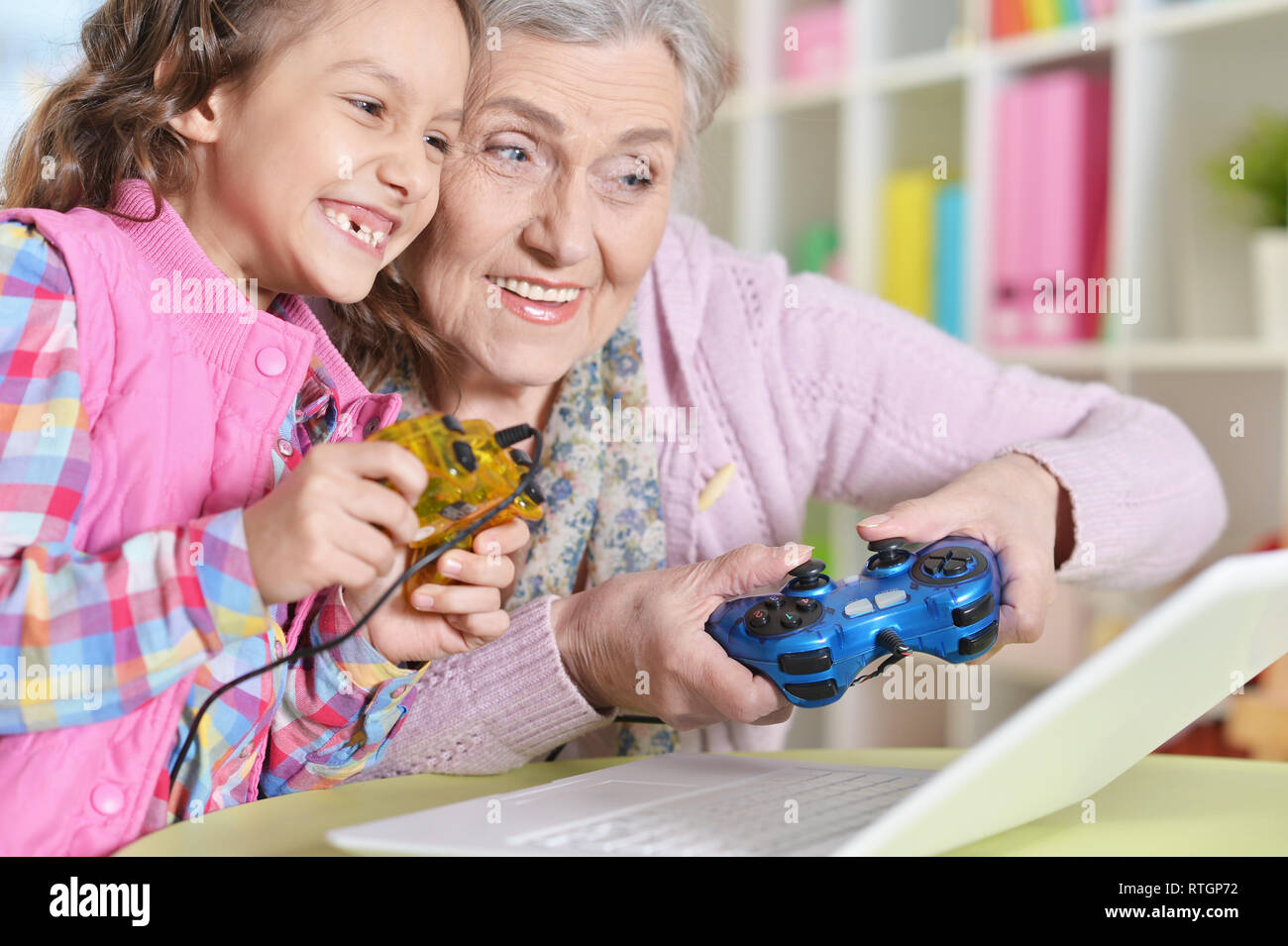 Portrait of granny with her granddaughter playing computer game on laptop Stock Photo