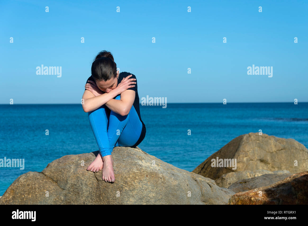 Depressed woman sitting on rocks by the sea Stock Photo