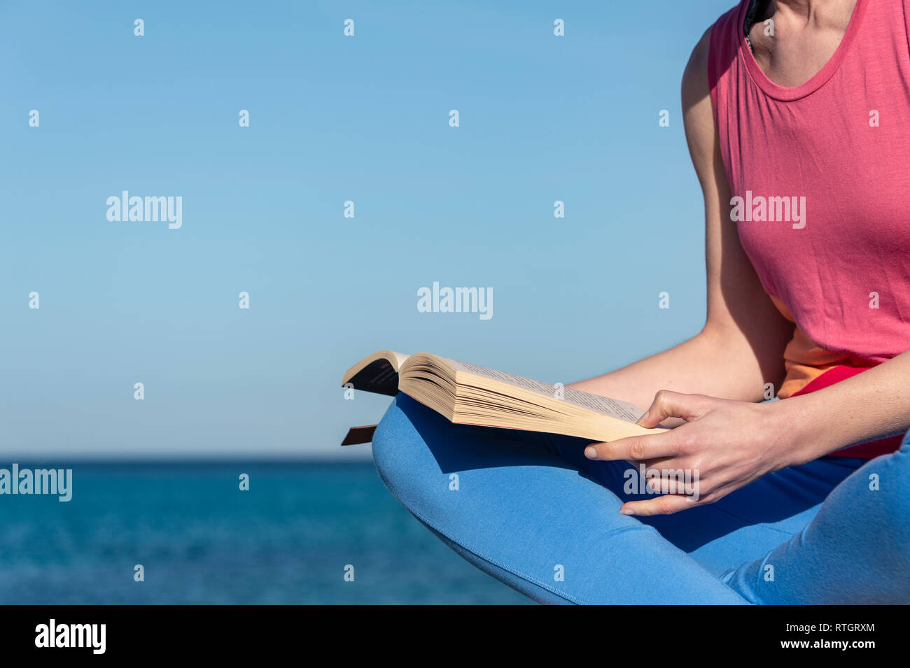 closeup of a woman reading a paperback book by the sea in the sun Stock Photo