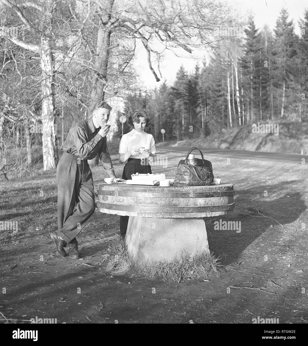 Lifestyle in the 1950s. A young couple has stopped to have a coffee and fika time a sandwich by the roadside. An old millstone makes a good table for the picnic. Photo Kristoffersson Ref BF76-4. Sweden 1952 Stock Photo