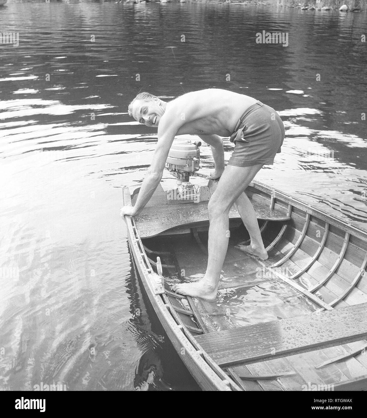 Boatlife in the 1950s. A man is trying to start the outboard engine on his boat. He also needs to empty it from the rain water as it is full of it. His name is Gustaf Wally, 1905-1966. Cousin to swedish diplomat Raoul Wallenberg who disappeared in Hungary 1945. Photo Kristoffersson ref BX20-7 Sweden 1950s Stock Photo