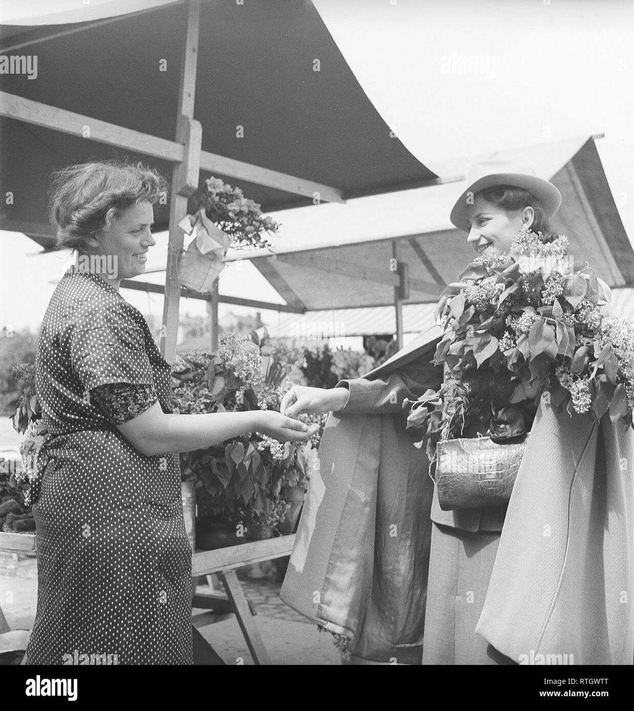 At the market in the 1940s. The young model and ballet dancer Gina Ohlsson at the flower market. She has just purchased a bouquet of syringa and pays the lady at the market stall. Photo Kristoffersson. Ref 134-1. Sweden June 1940 Stock Photo