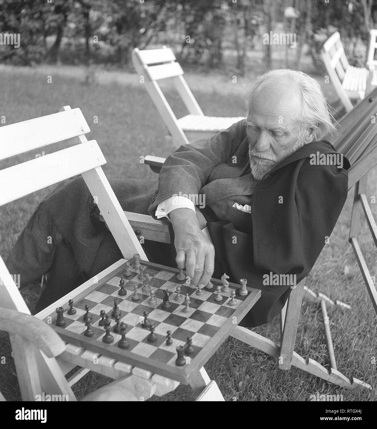 Chess player in the 1950s. An elderly man in an comfortable garden chair is playing chess with someone, and makes a move on the chess board. Photo Kristoffersson Ref BE21-9. Sweden 1952 Stock Photo