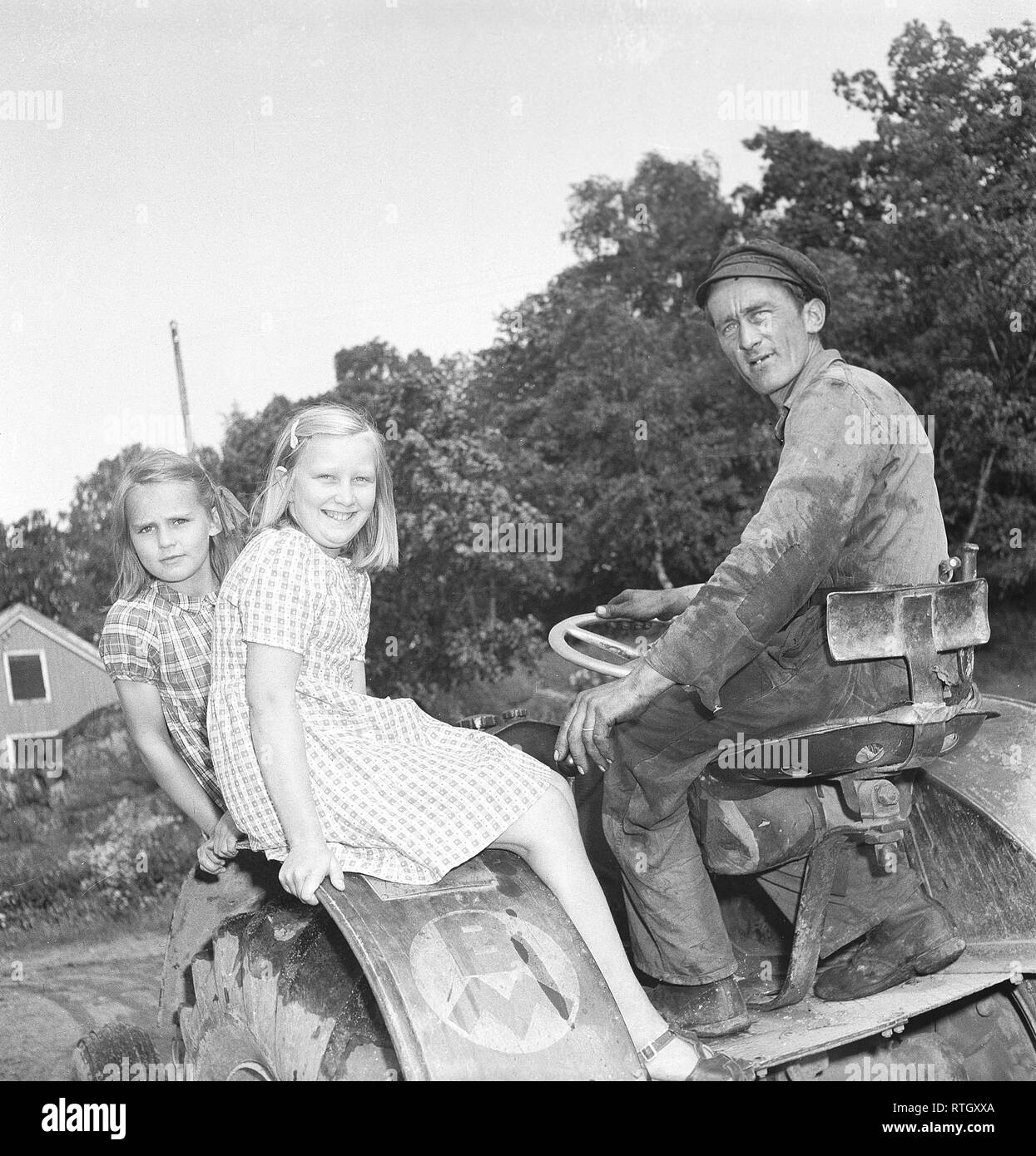 Summer in the 1940s. Two girls in summer dresses are enjoying the summer day in the country. Perhaps on a summer holiday in the countryside where they enjoy riding on the tractor.  Photo Kristoffersson. Ref U54-3. Sweden 1946 Stock Photo