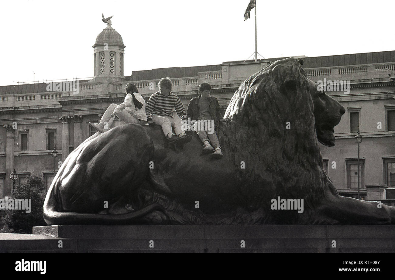 1970s, three teenage boys sitting on the back of one of the lion statues at Trafalgar Square, London, England, UK. The large bronze lions, designed by Sir Edwin Landseer and installed in 1867 to guard Nelson's Column, are a famous landmark in the city and a great place to climb up on and take in the view. Stock Photo