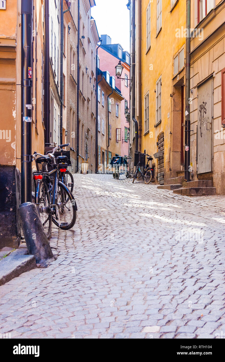 Stockholm, Sweden - May 26, 2017: Cozy medieval paving stone street with parked bicycles, working businesses, yellow orange red buildings facades in G Stock Photo